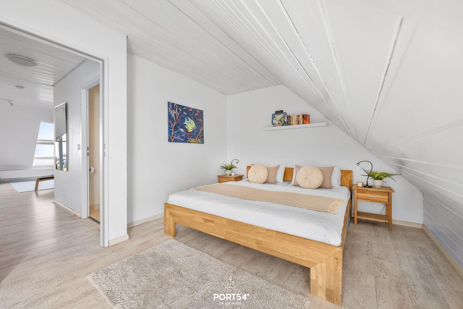 Schlafzimmer mit Holzbett, Nachttischen und Wandbild. Dachschrägen und Holzboden.
