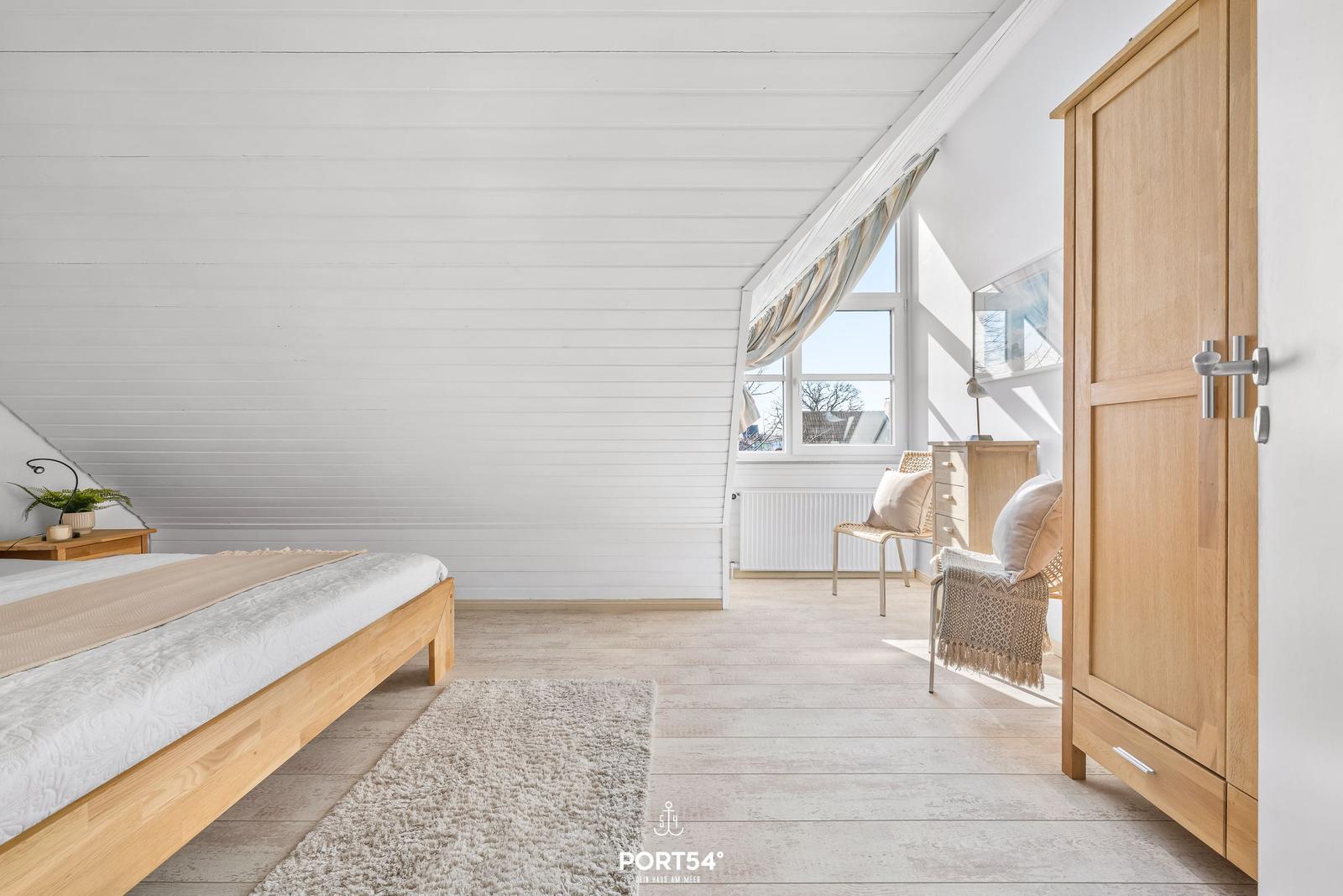 Schlafzimmer mit Holzbett, Kleiderschrank und Fenster mit Blick.