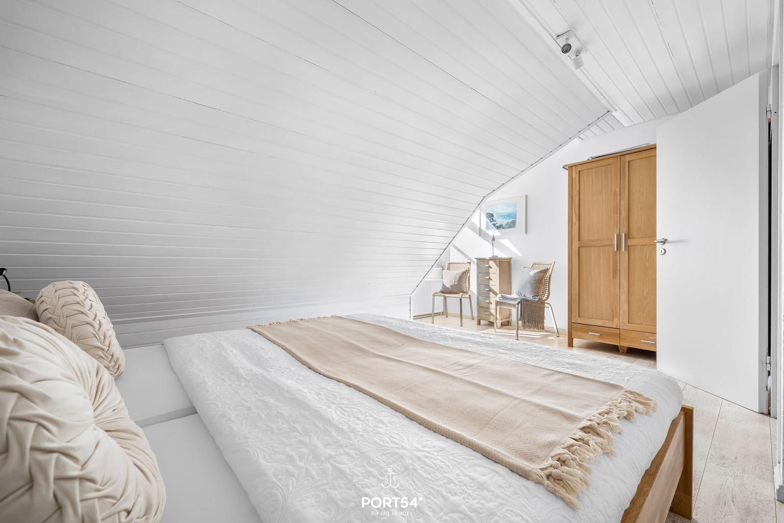Schlafzimmer mit Dachschrägen, Bett, Kleiderschrank und Stühlen.