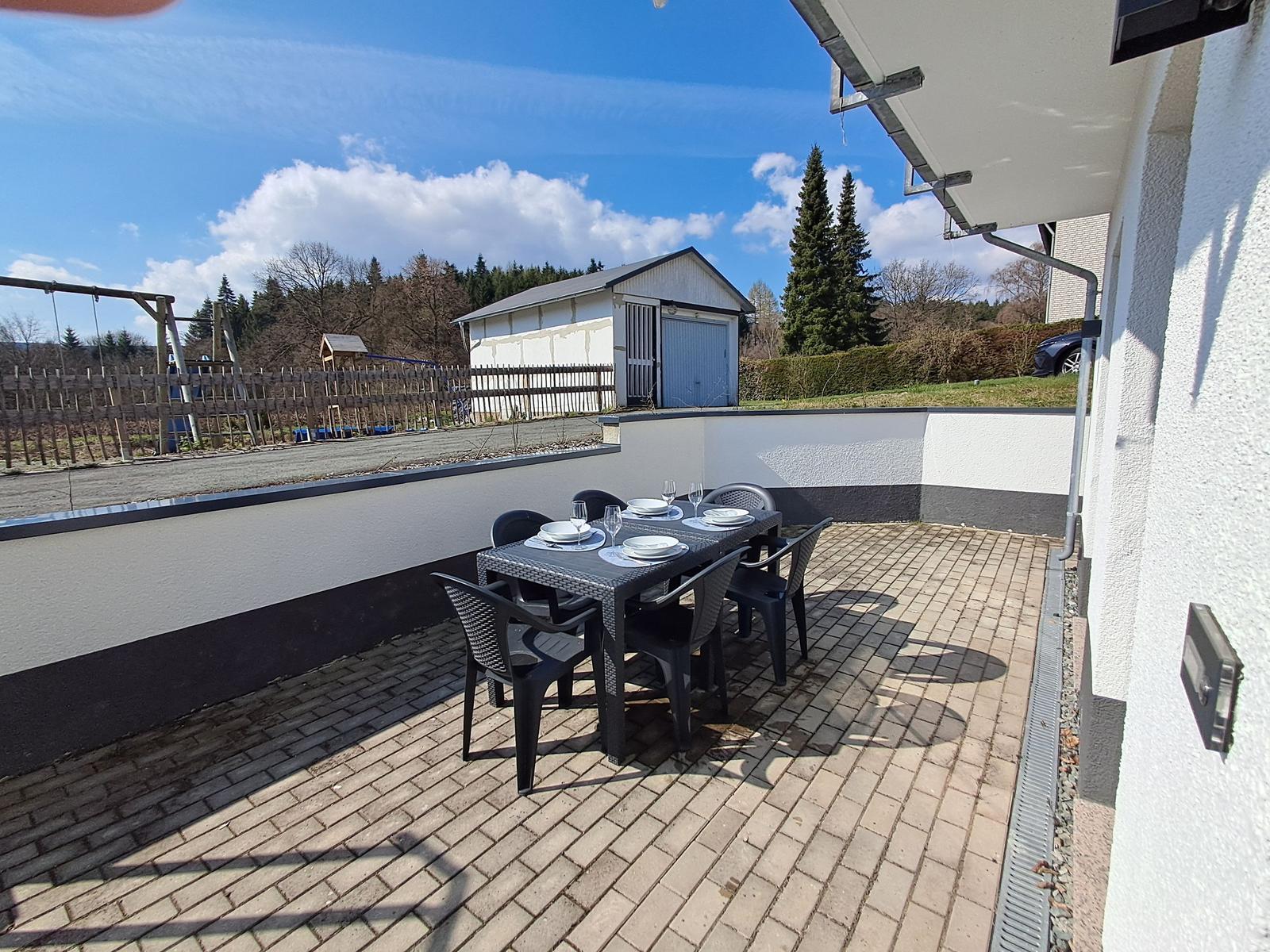 Terrasse mit Tisch und Stühlen, Blick auf Garten und Garage.