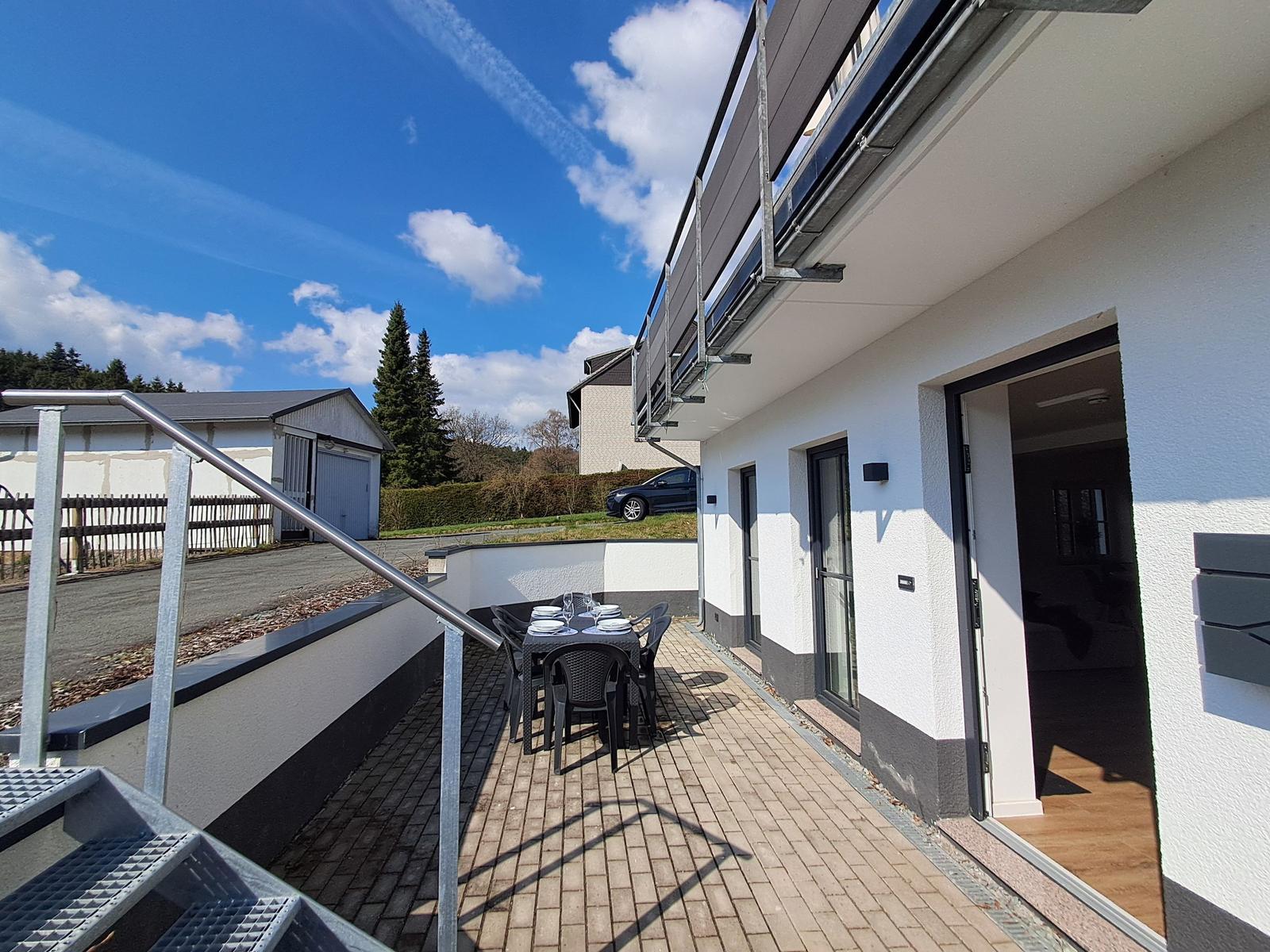 Terrasse mit Tisch und Stühlen neben Wohnhaus mit Eingang.