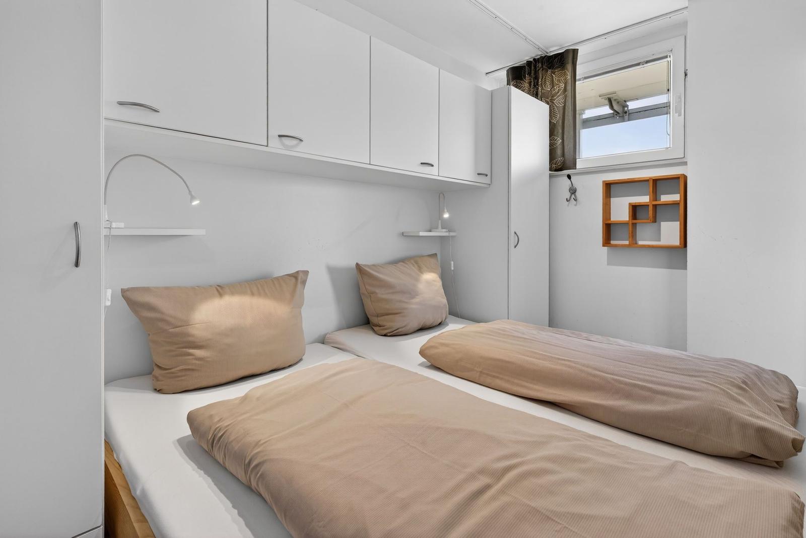 Two beds with beige bedding, white cabinets, and a small window.