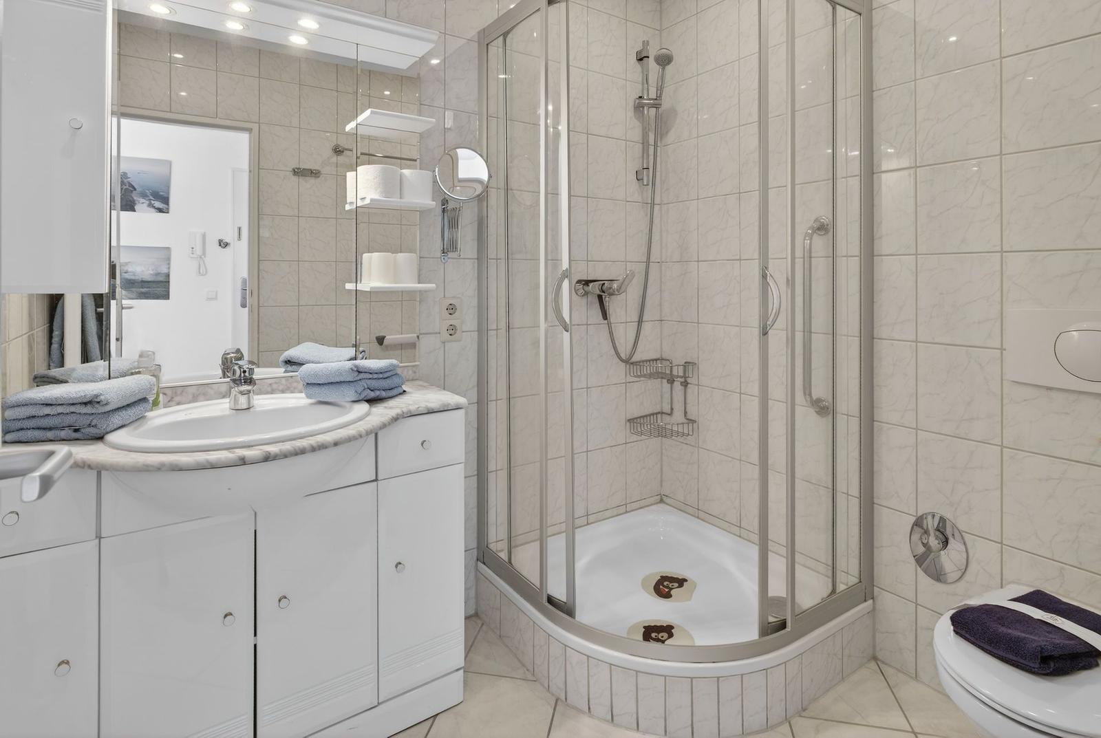 Bathroom with shower, sink, and toilet. Tiles and white fixtures.