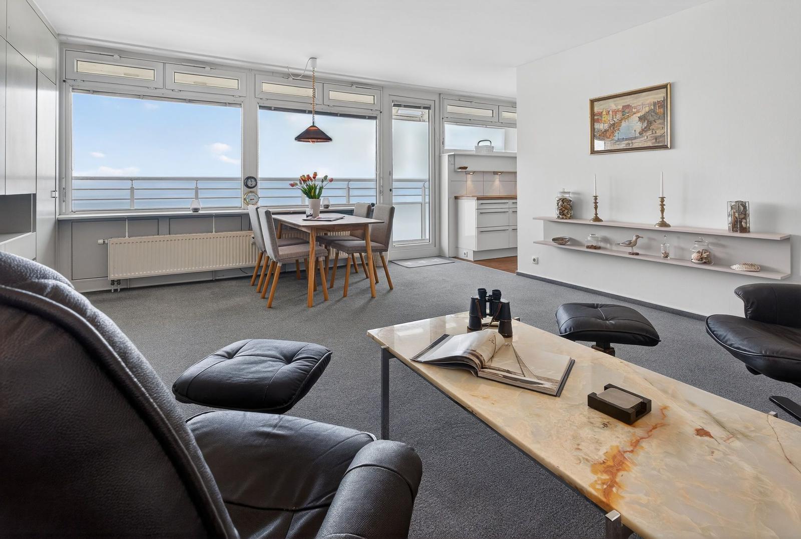 Living area with dining space, large windows, and sea view. Table, chairs, sofa, and coffee table.