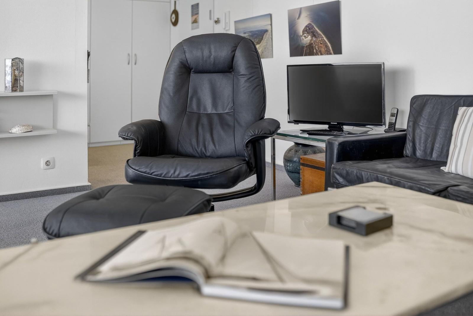 Black leather recliner with footrest, TV, and sofa in the living room.