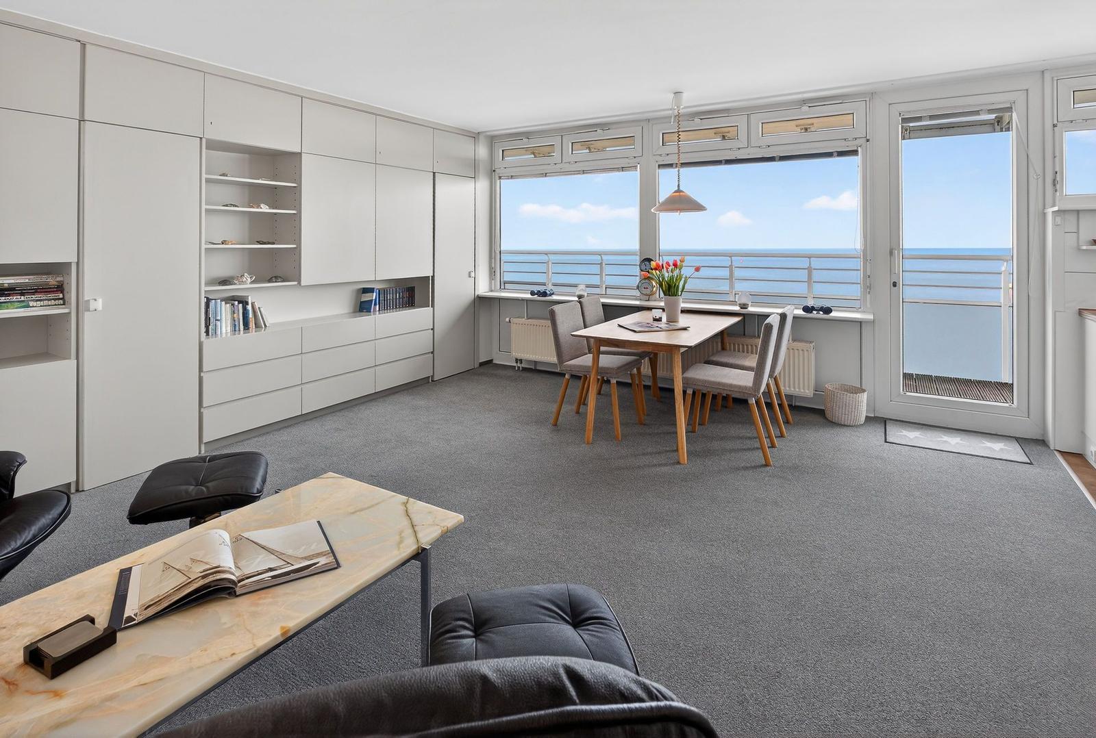 Living and dining area with sea view, dining table, bookshelves, and terrace door.
