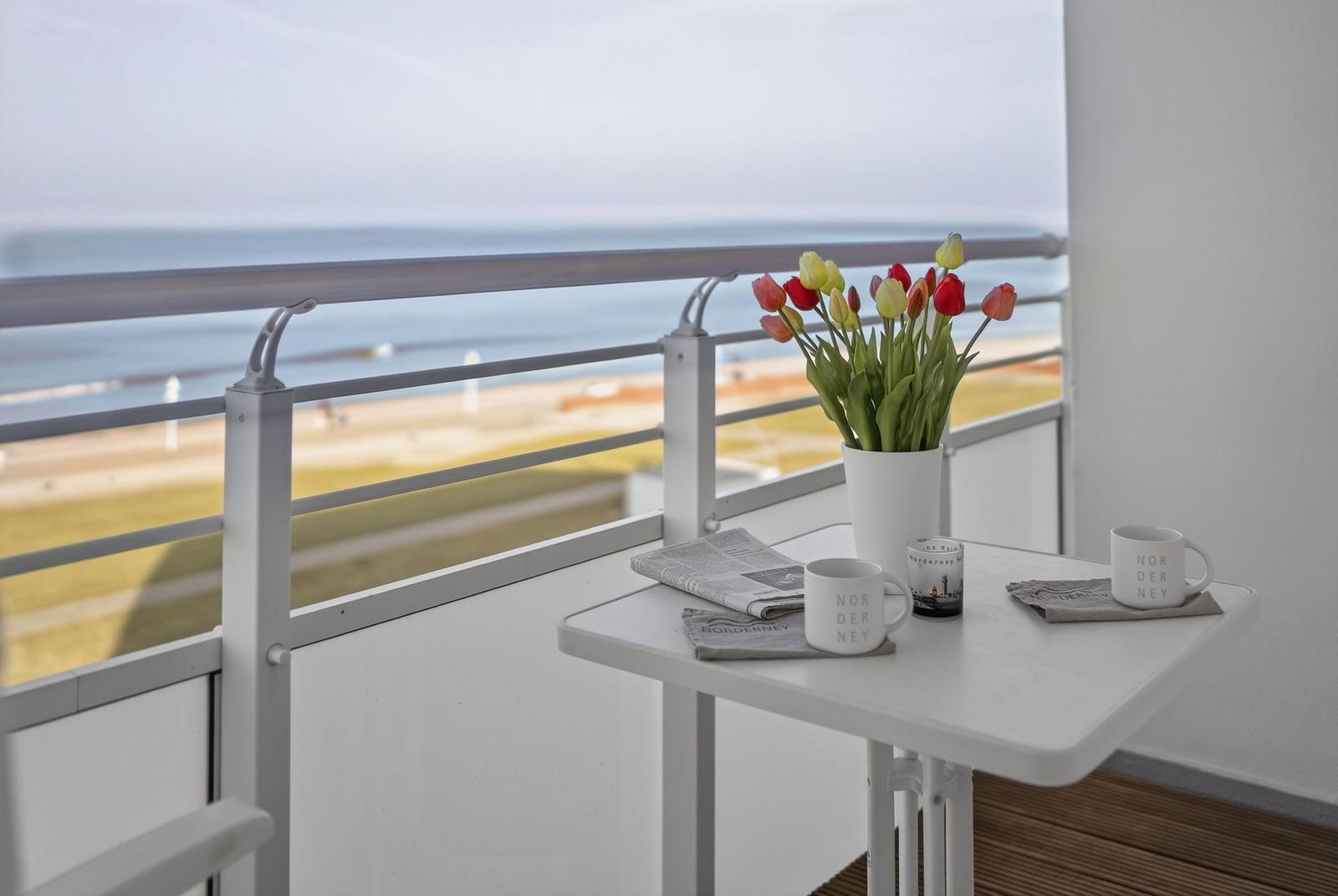 Balcony with table, flowers, and sea view.