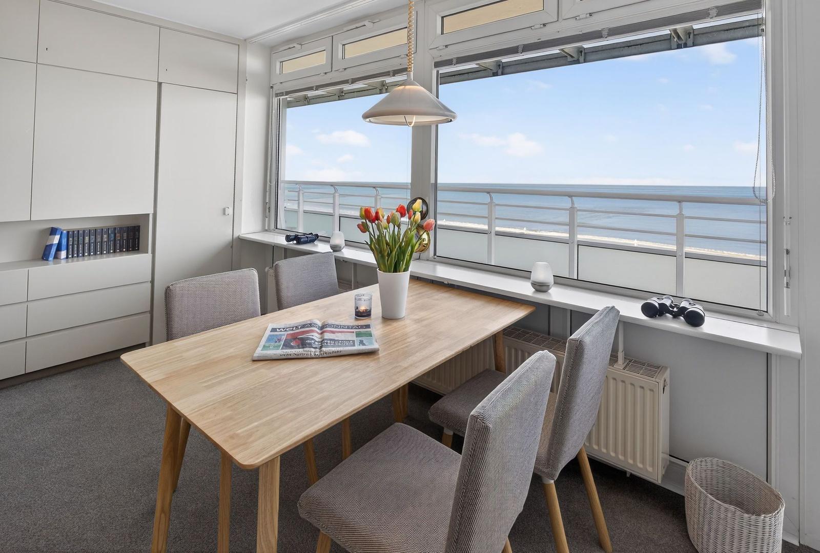 Dining room with sea view, wooden table, chairs, flowers, and windowsill.