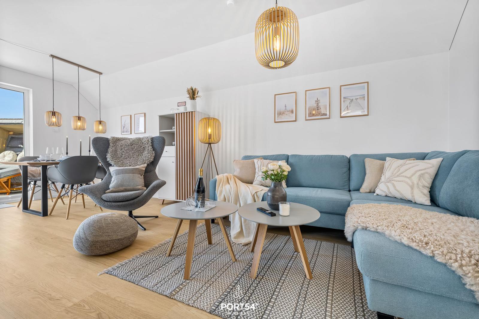 Ein Wohn- und Essbereich mit blauem Sofa, grauer Sessel und Holzboden.