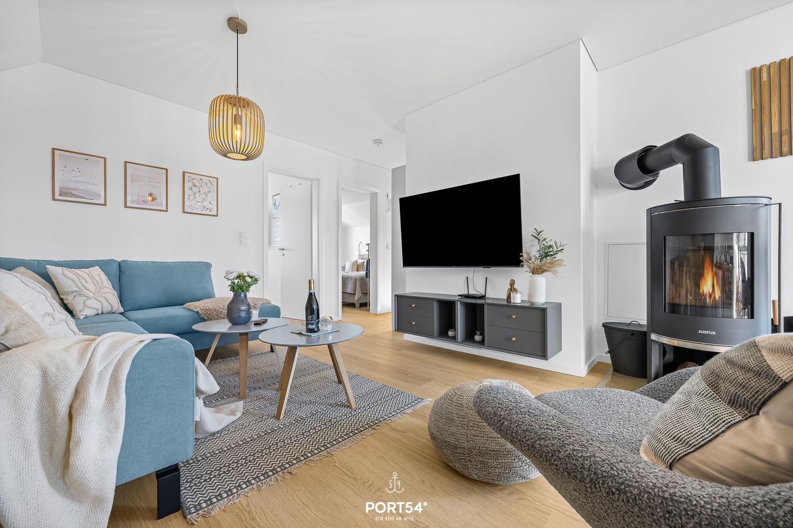 Wohnzimmer mit Sofa, Fernseher und Kaminofen. Holzboden und helle Wände.
