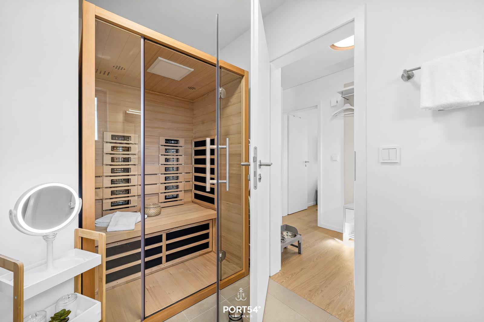 Innenraum einer Sauna mit Holzverkleidung und Glasfront. Nebenraum mit Kleiderständer und Bodenbelag.