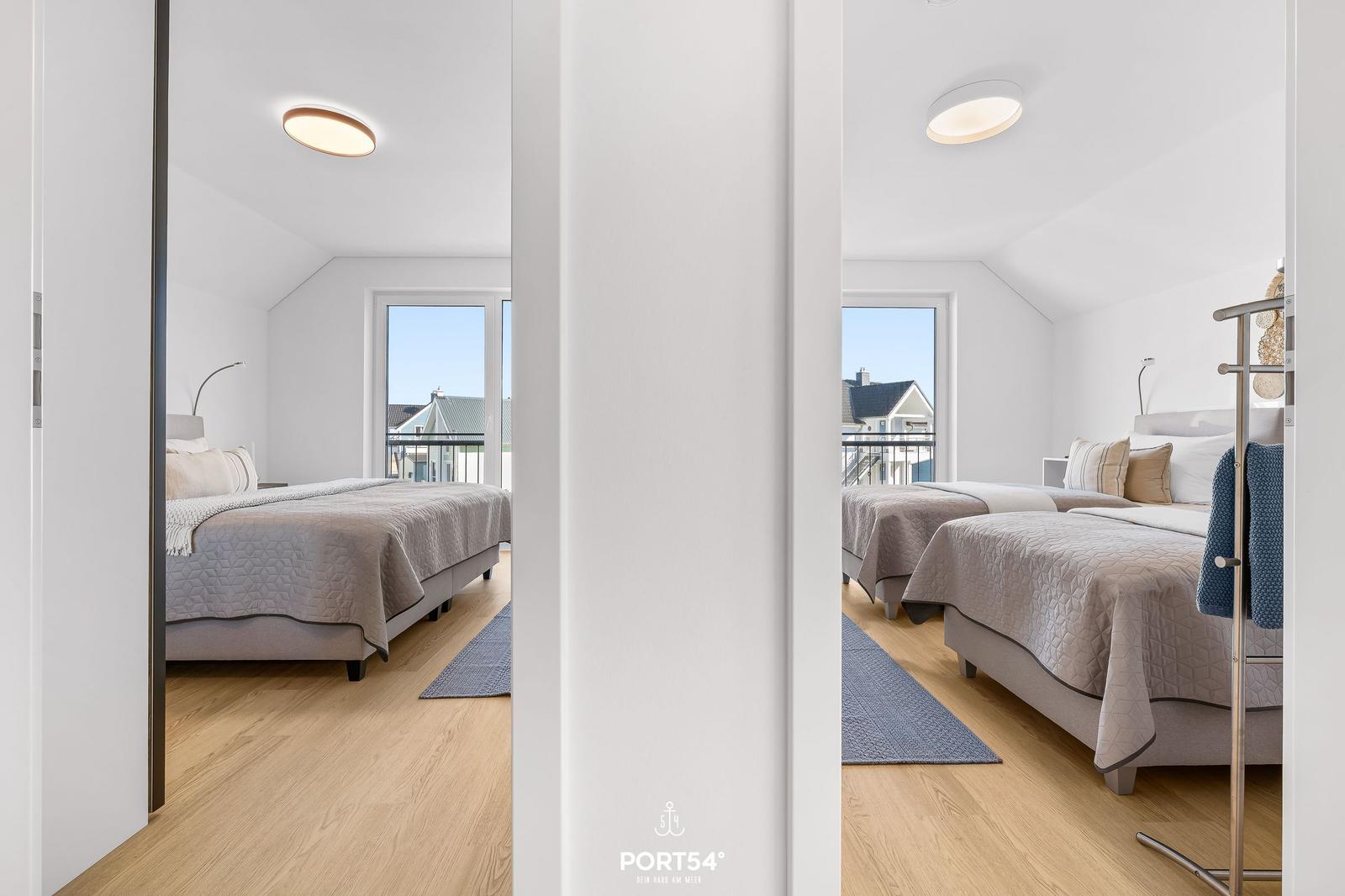 Zwei Schlafzimmer mit Doppelbetten, Holzboden und Fenster zum Balkon.