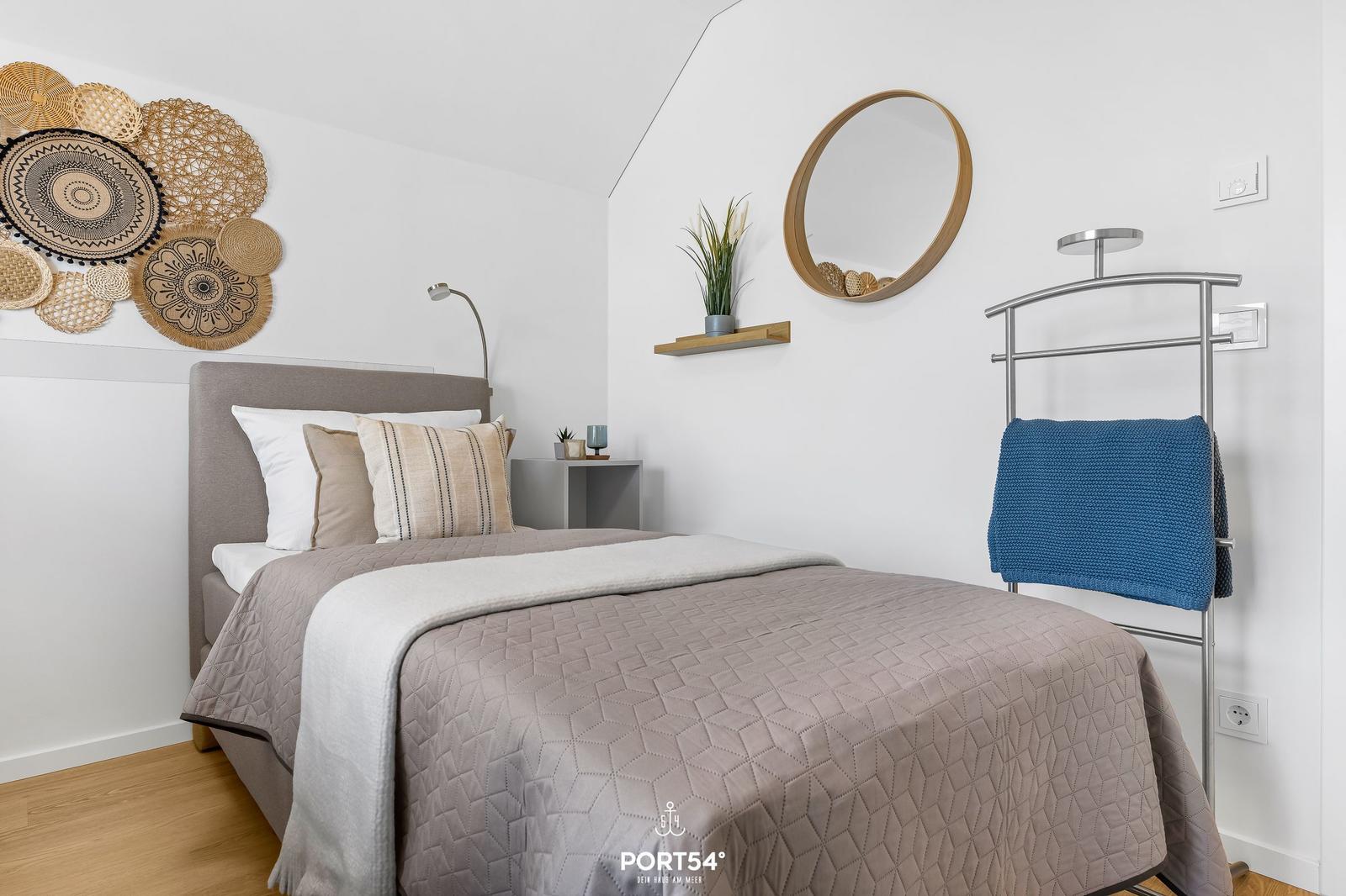 Schlafzimmer mit Bett, Wanddekoration, Spiegel und Handtuchständer.