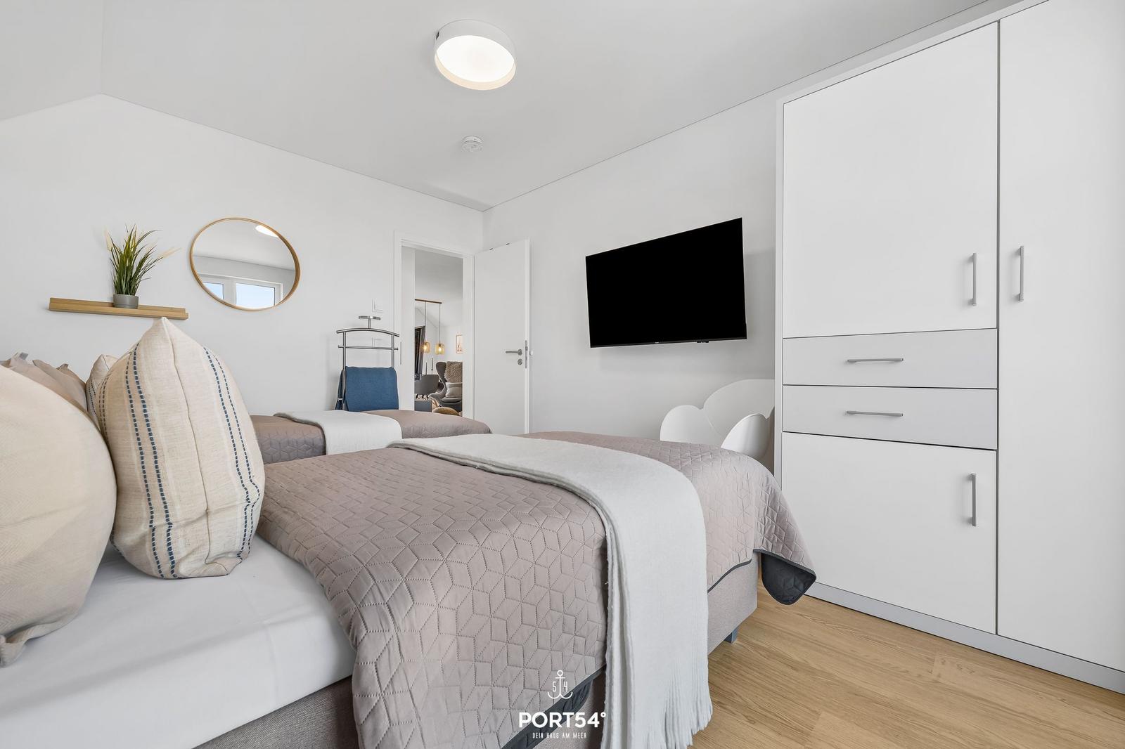 Zimmer mit zwei Betten, Kleiderschrank und Wandfernseher.