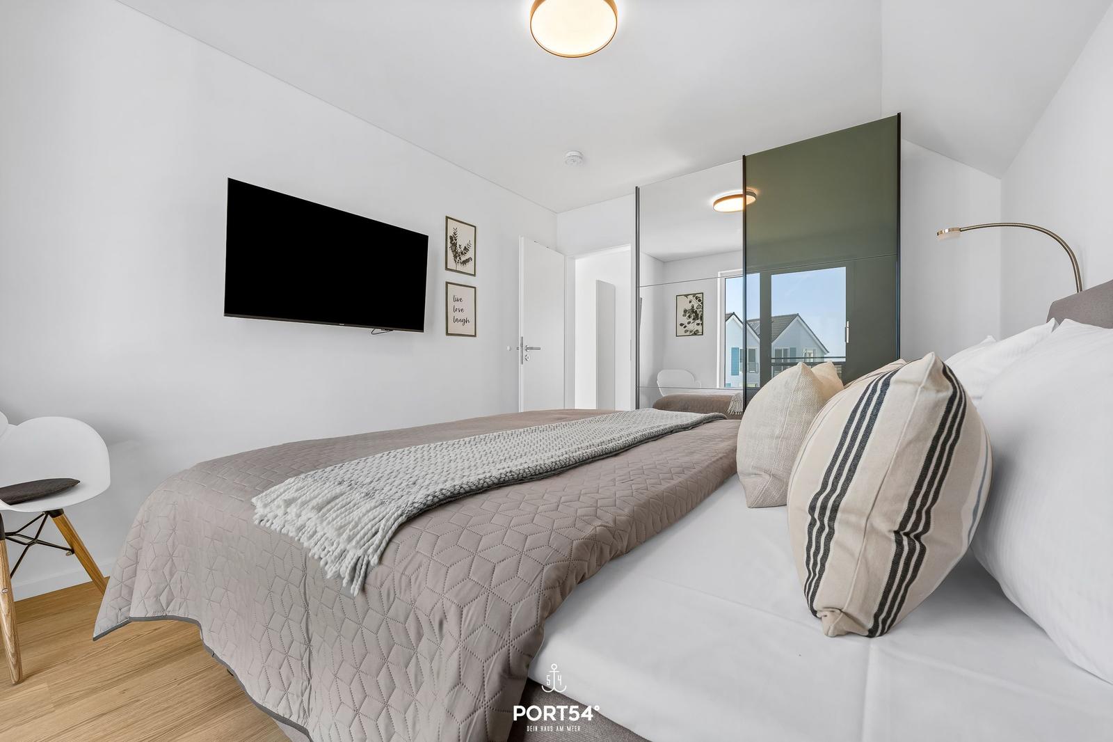 Schlafzimmer mit Bett, Fernseher und Spiegelschrank. Blick auf Balkon.