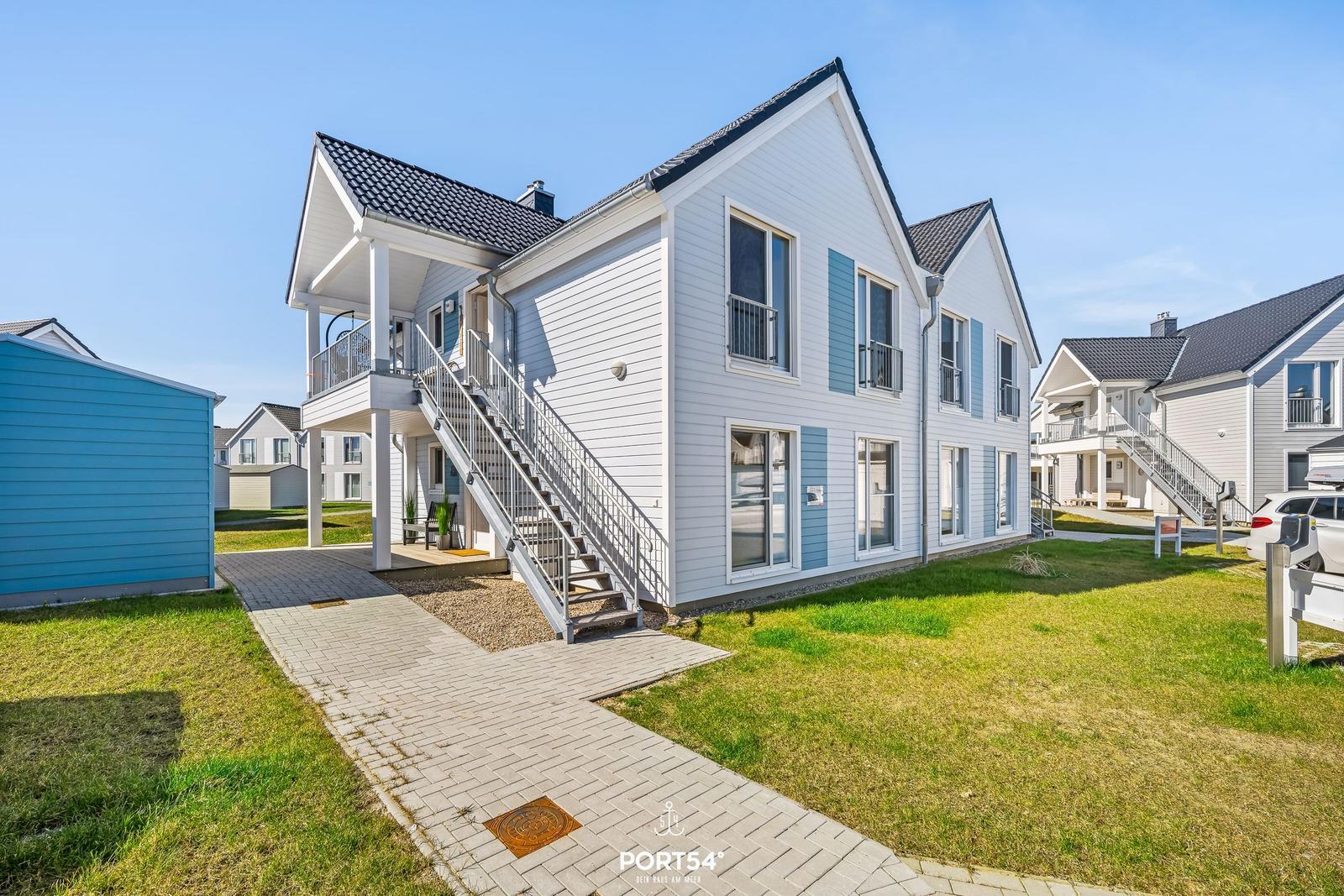 Ein zweistöckiges Haus mit Balkon und Außentreppe. Grünfläche und gepflasterter Weg.