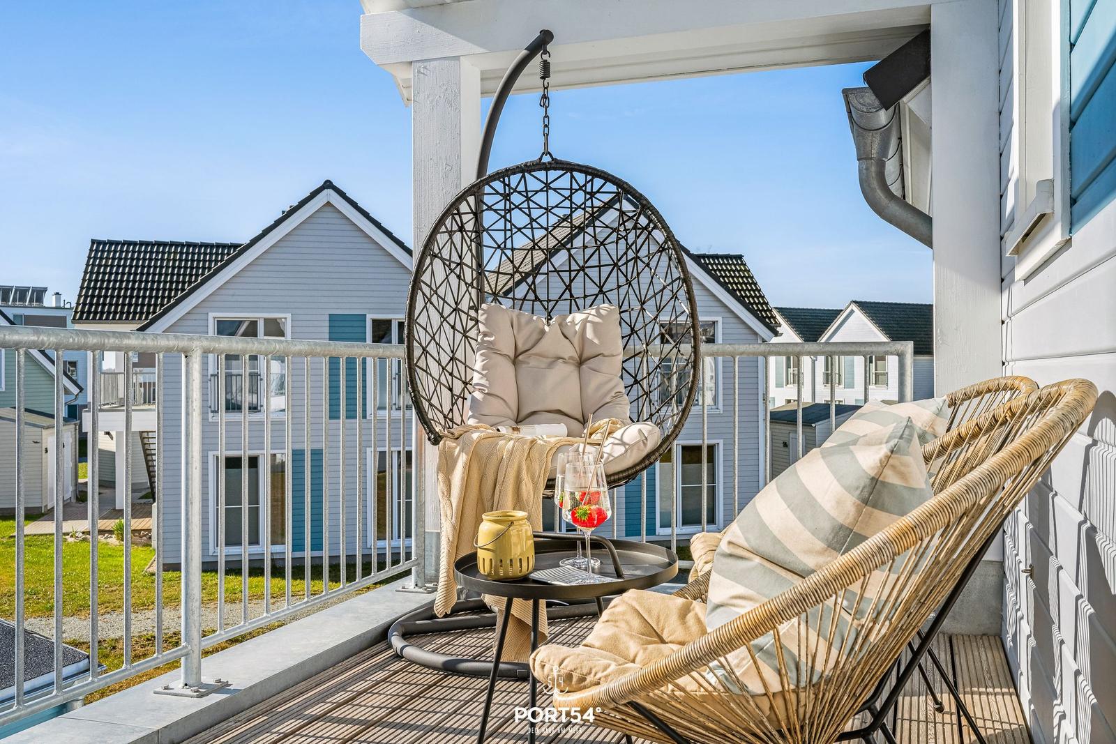 Terrasse mit Hängesessel und Rattanstühlen. Blick auf Nachbarhäuser.