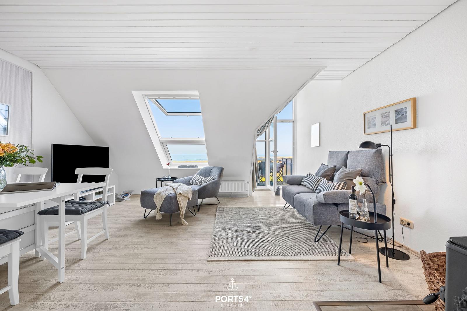 Wohnzimmer mit Sofa, Sessel und TV. Dachfenster und Balkon mit Meerblick.