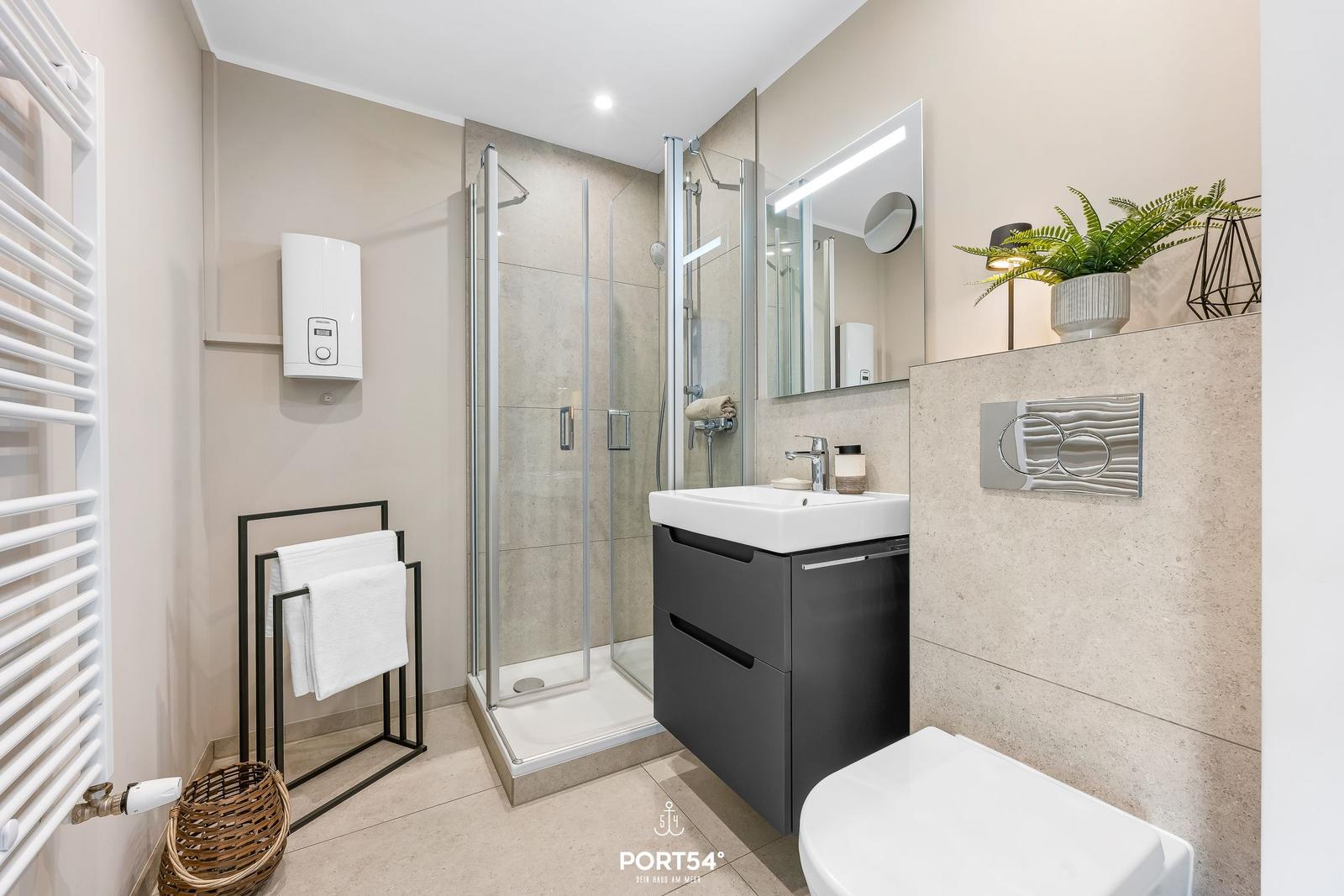 Badezimmer mit Dusche, Waschbecken und Toilette. Modern eingerichtet mit Pflanze und Handtuchhalter.