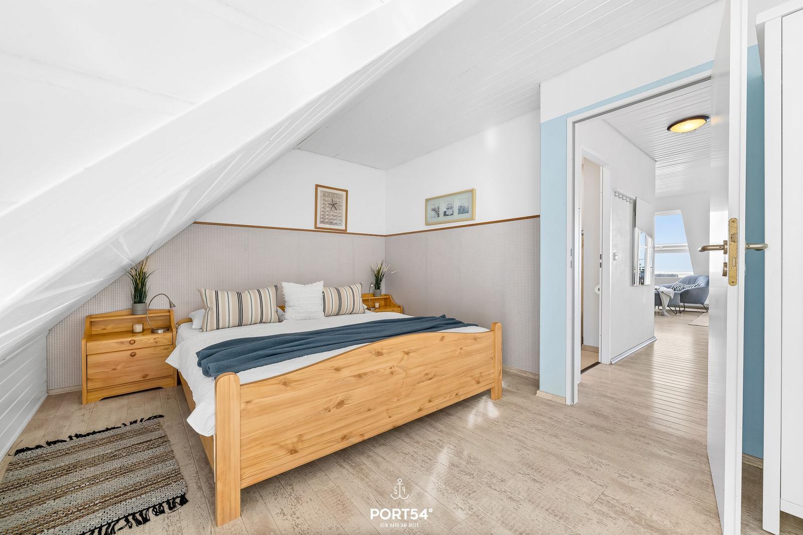 Schlafzimmer mit Holzbett, Nachttischen und Blick in Wohnbereich.