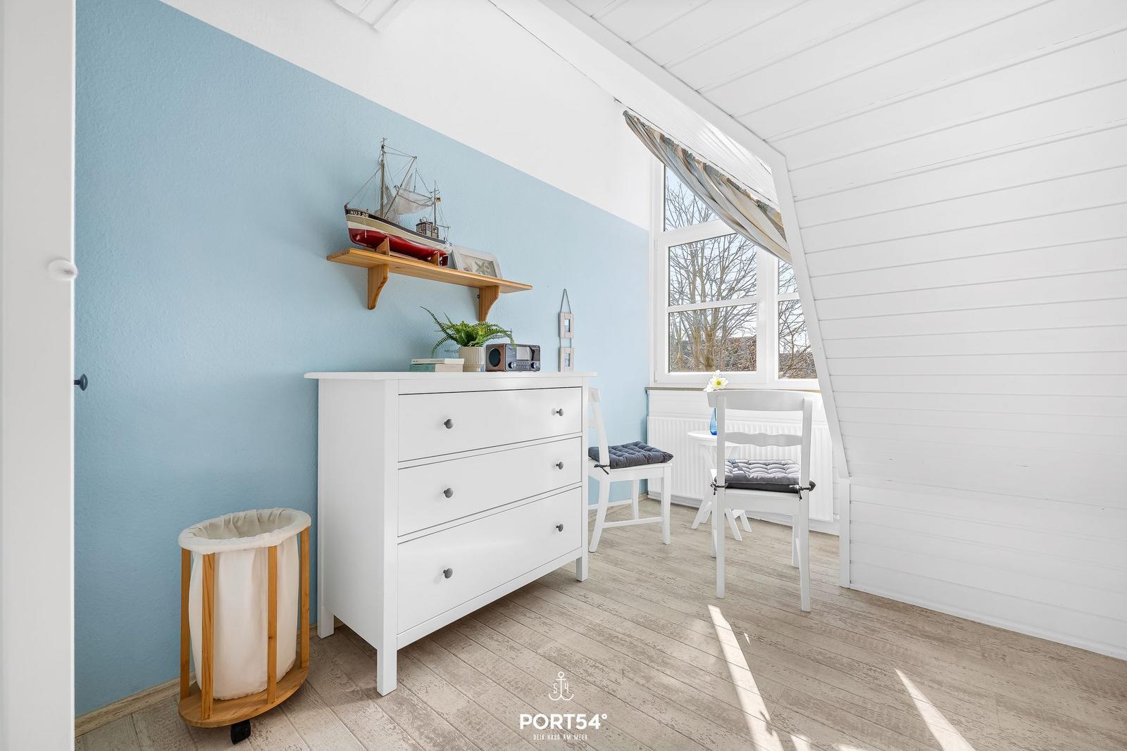 Ein Raum mit blauer Wand, weißem Schrank und Fenster mit Blick nach draußen.