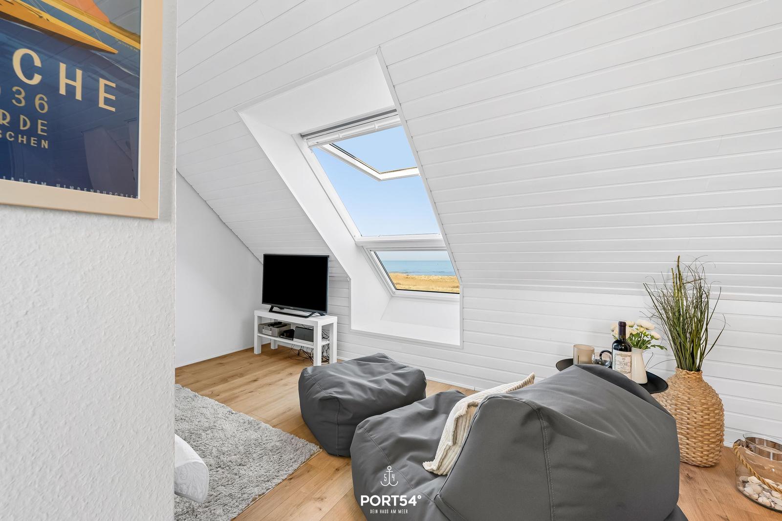 Dachgeschosszimmer mit TV, Sitzgelegenheit und Blick aufs Meer.