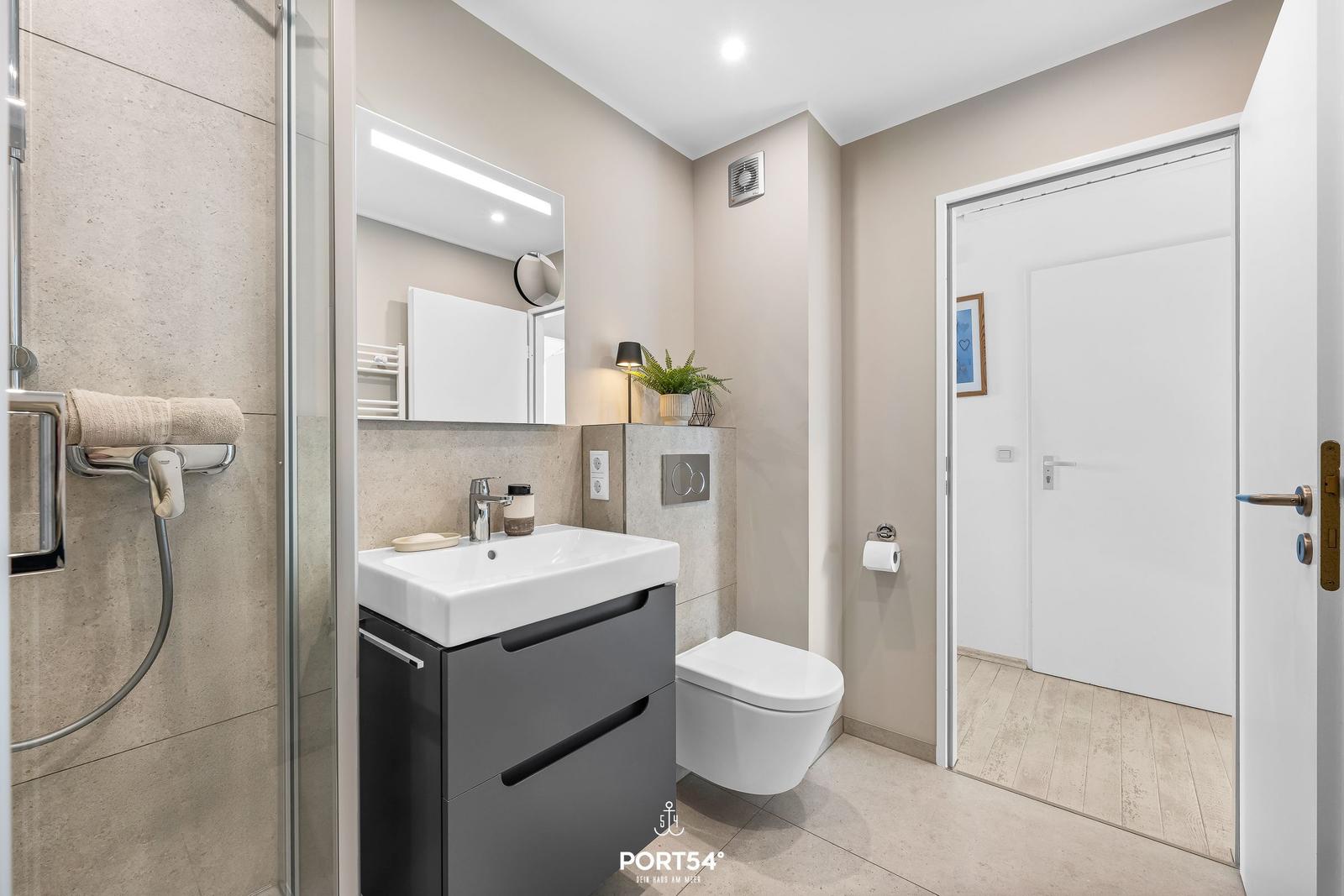 Badezimmer mit Dusche, Waschbecken und Toilette. Moderne Einrichtung mit Spiegel und Pflanze.
