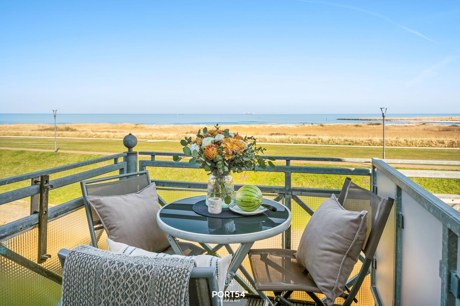 Terrasse mit Tisch, Stühlen und Blick auf Meer und Wiese.