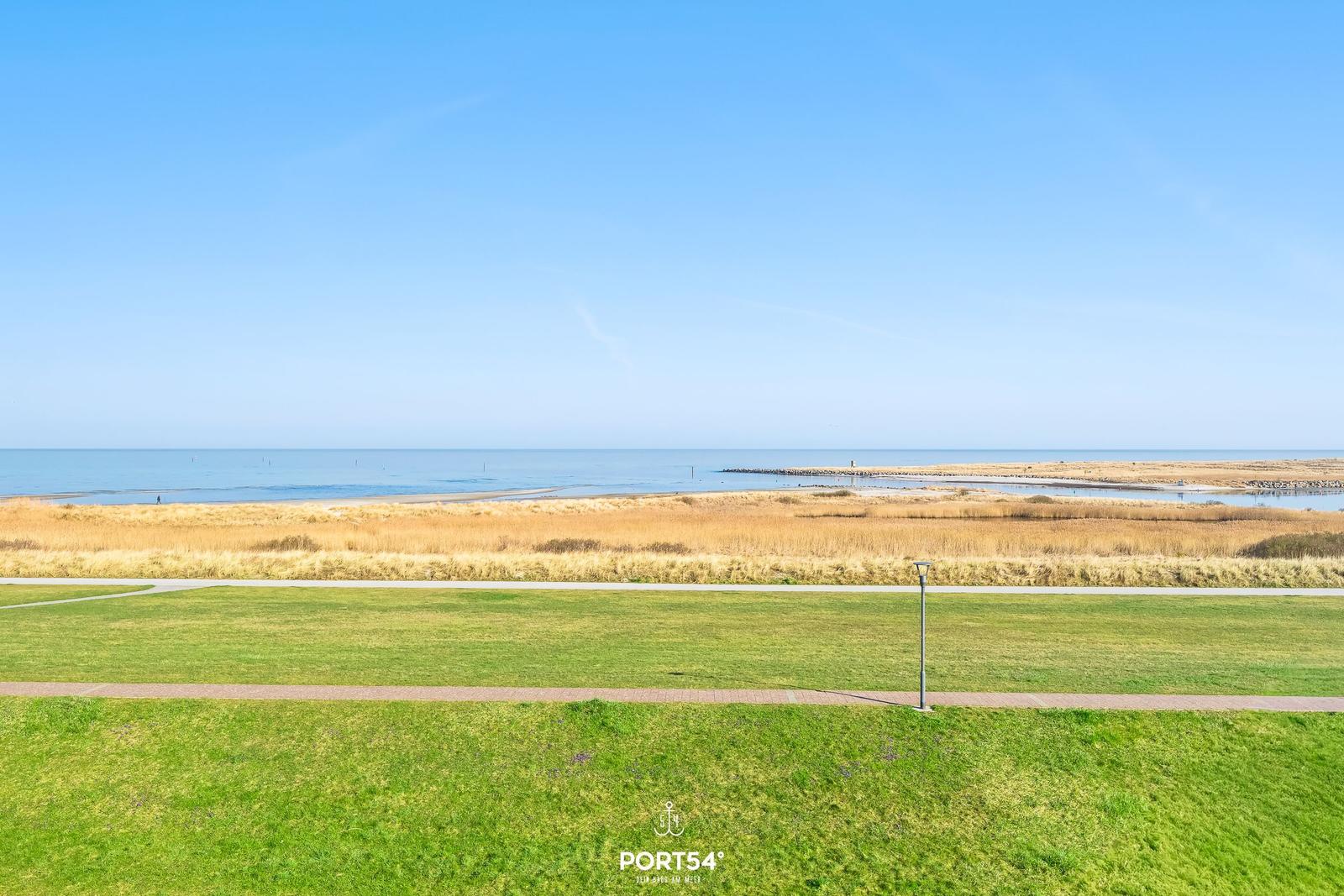 Weitläufiger Blick auf Strand und Grünflächen unter klarem Himmel.