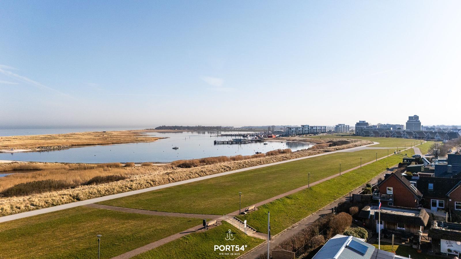 Weitläufiger Blick auf Hafen, Grünflächen und moderne Gebäude am Wasser.