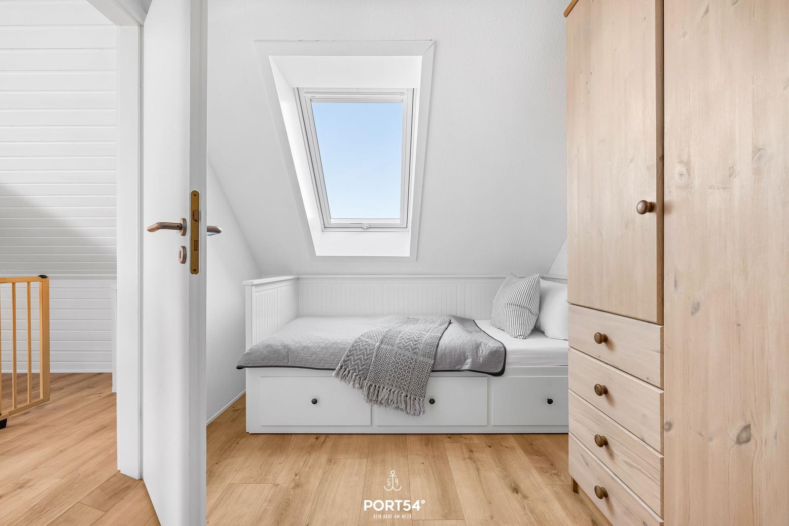 Dachgeschosszimmer mit Dachschrägen, Dachfenster und weißem Bett mit Holzschrank.