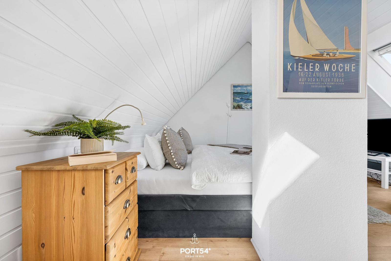 Schlafzimmer mit Dachschrägen, Holzkommode und Poster an der Wand.