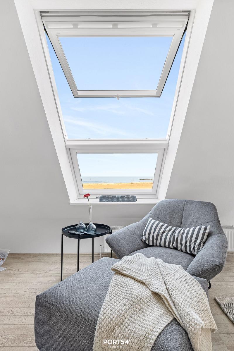 Dachfenster mit Meerblick, grauer Sessel und Beistelltisch.
