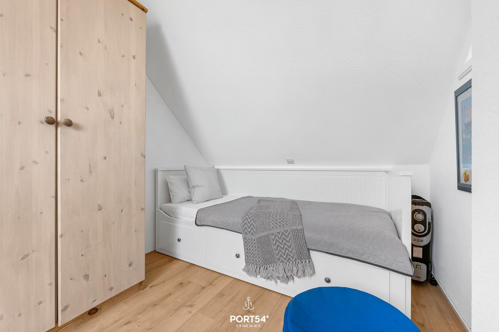 Schlafzimmer mit Dachschräge, weißem Bett und Holzschrank.