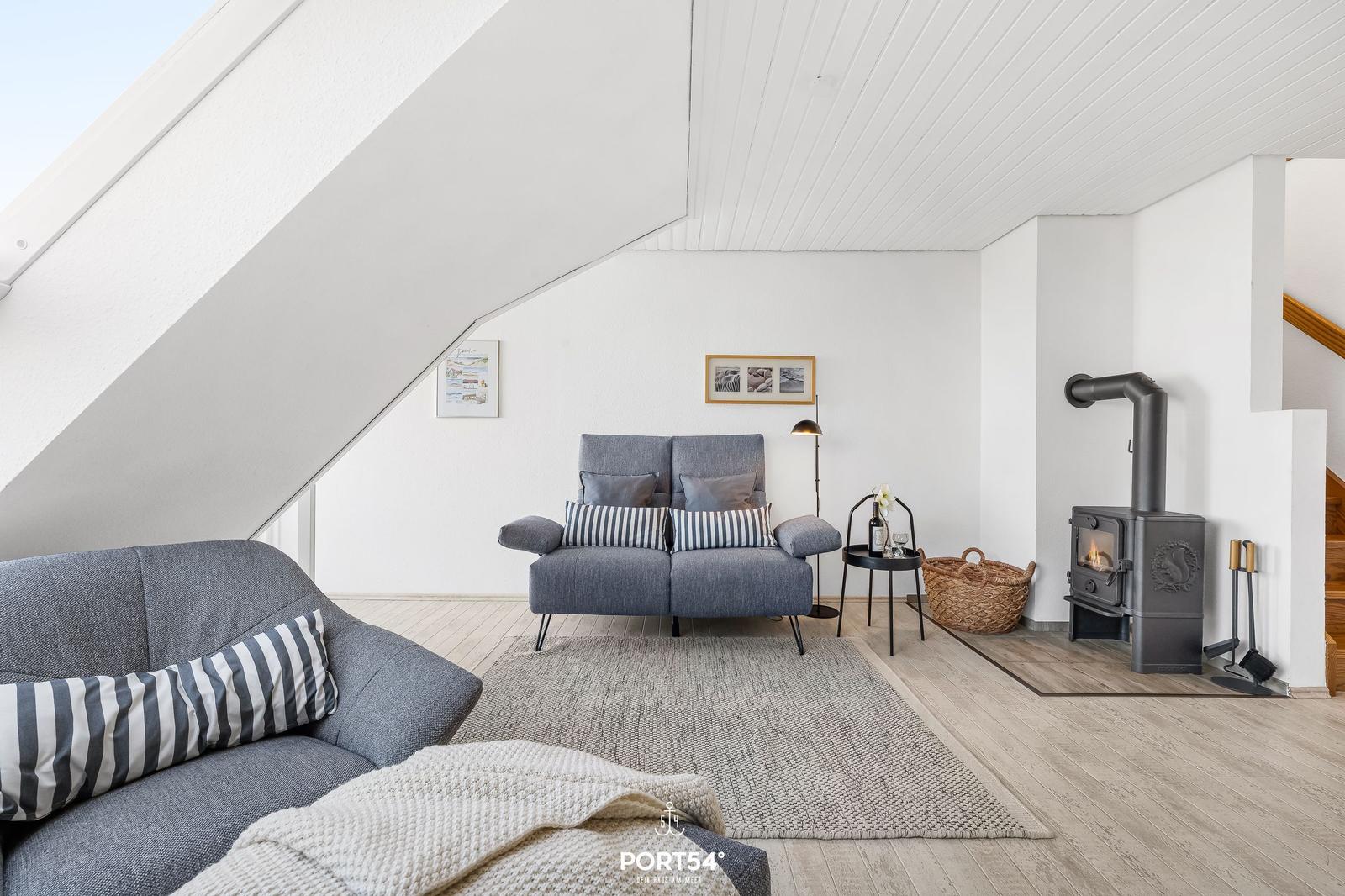 Wohnraum mit grauem Sofa, Kamin und Holzboden unter schrägen Dachdecken.