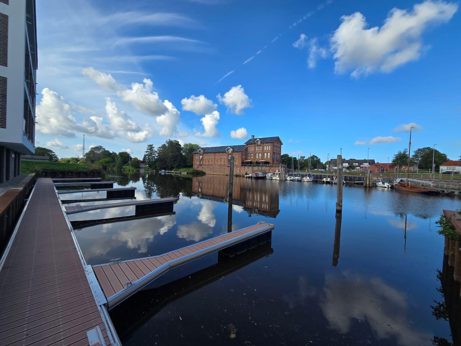 Hafen mit Booten und Reflexionen unter blauem Himmel mit weißen Wolken.