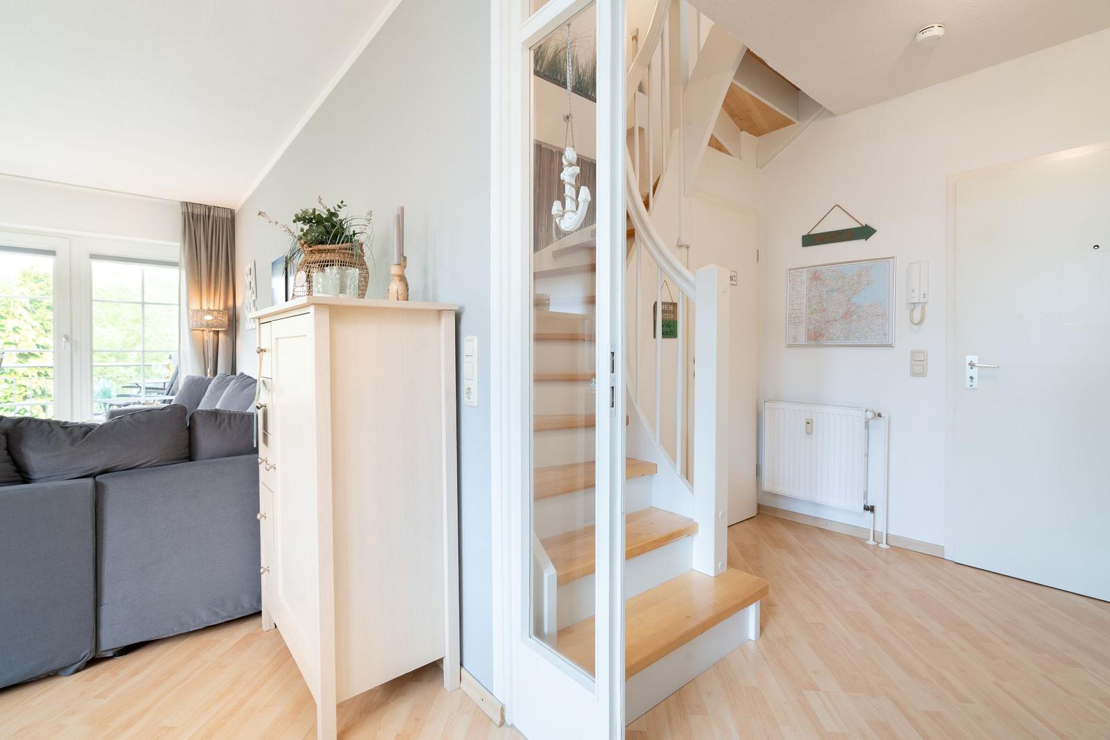 Eingangsbereich mit Treppe und Wohnzimmer mit Sofa und Fenster.