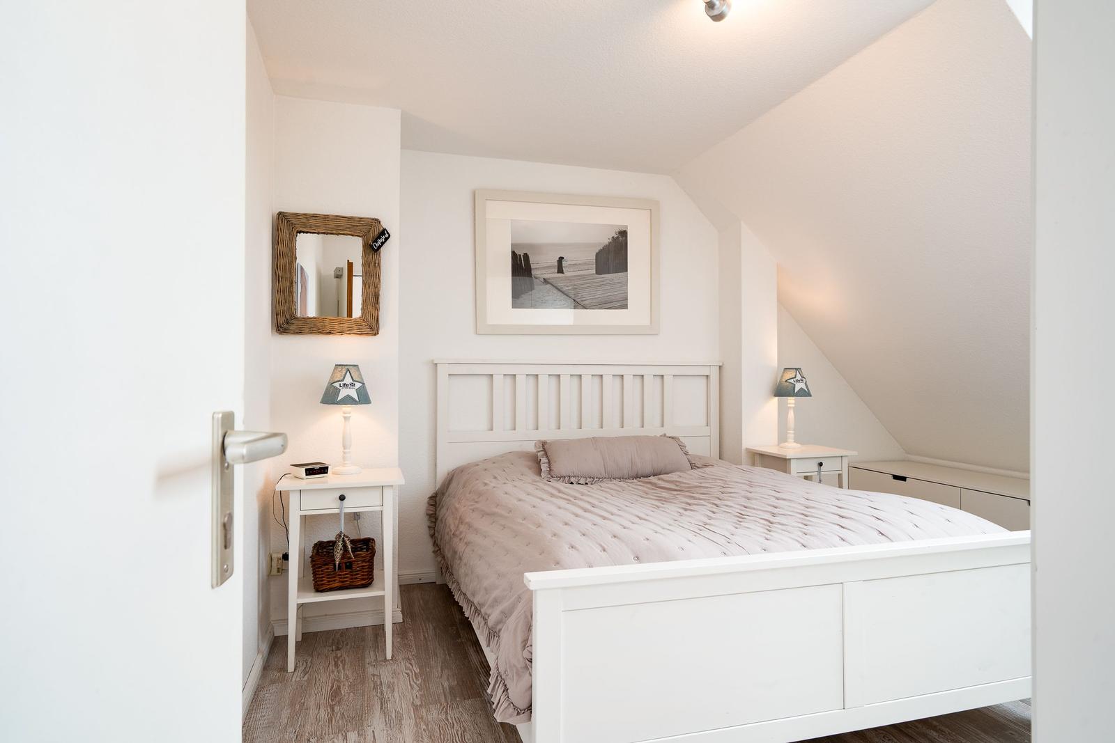 Schlafzimmer mit weißem Bett, Nachttischen und Wandbild unter Dachschrägen.