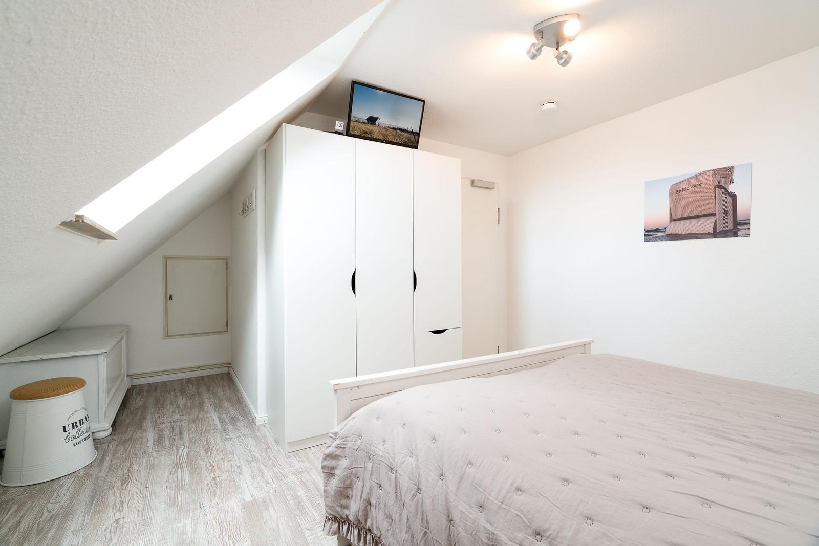 Schlafzimmer mit Dachschrägen, weißem Kleiderschrank und Bett mit gesteppter Bettdecke.