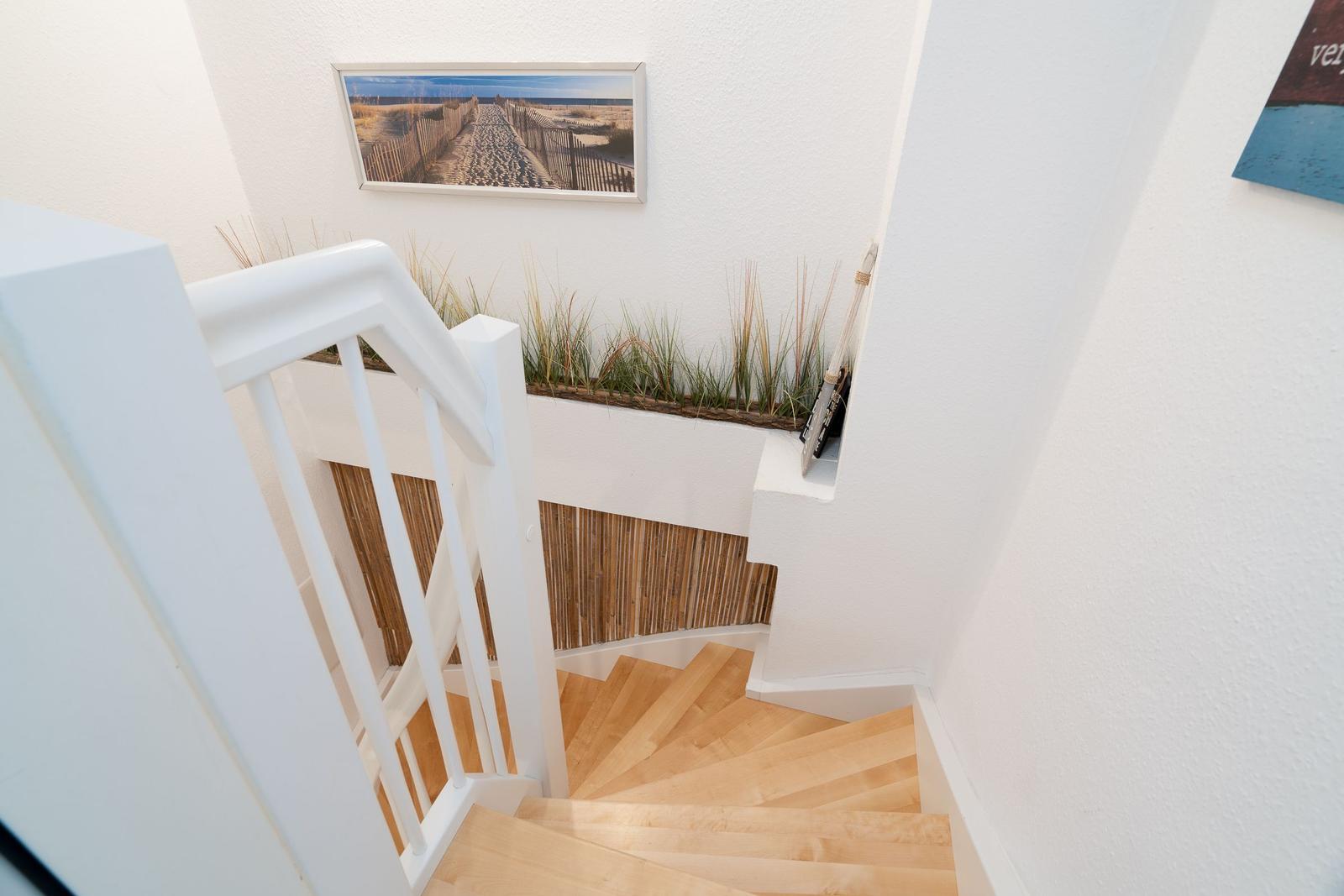Helle Treppe mit Holzstufen und weißem Geländer. Wandbild und Pflanzen im Hintergrund.
