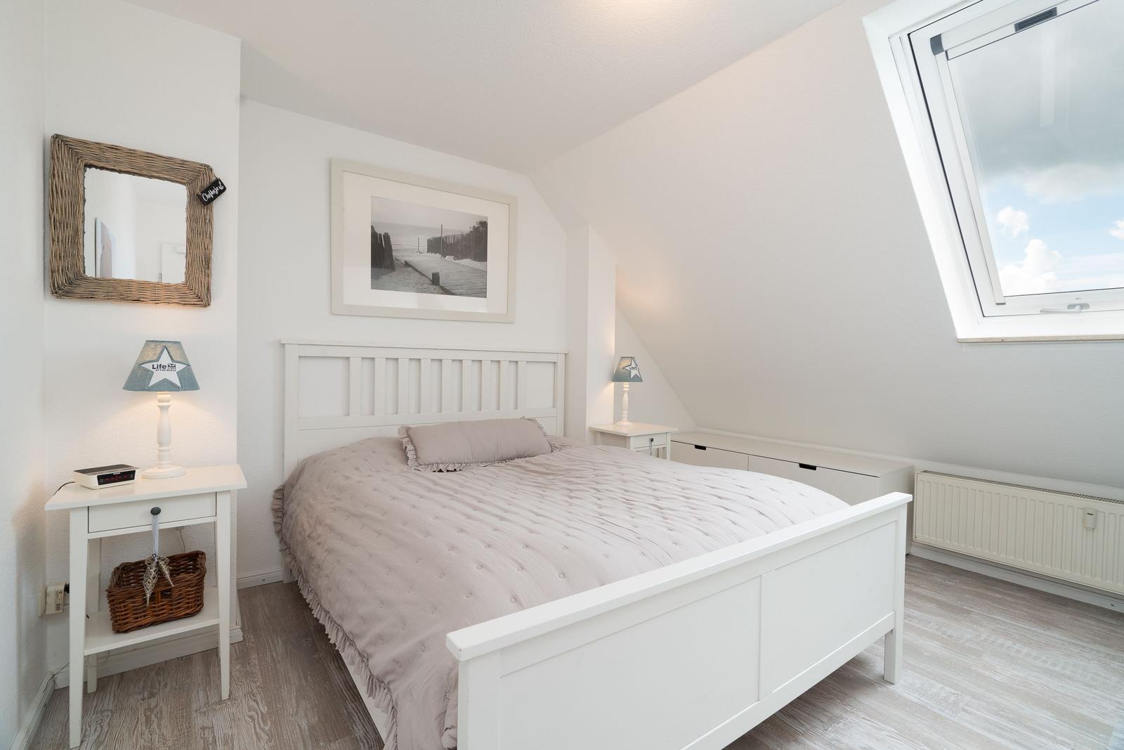 Schlafzimmer mit Dachschräge, großem Bett und Dachfenster. Weiße Einrichtung und Holzboden.