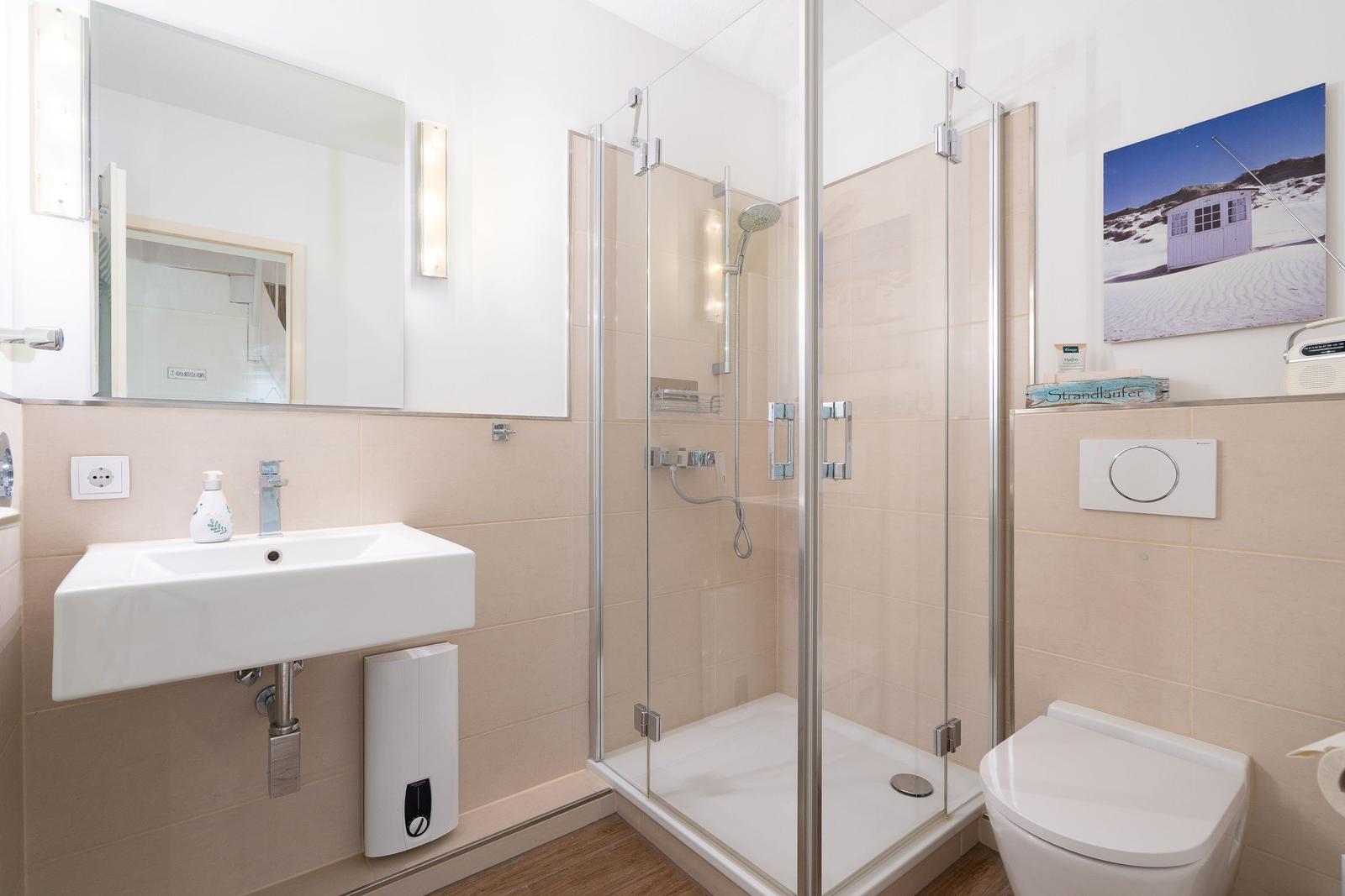 Bad mit Dusche, Waschbecken und Toilette. Wandbild und Spiegel sind sichtbar.