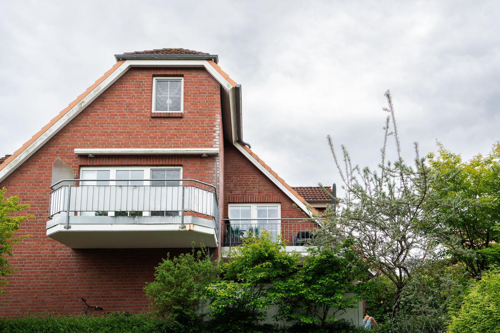 Rotes Backsteinhaus mit Balkon und Dachfenster. Umgeben von grüner Vegetation.