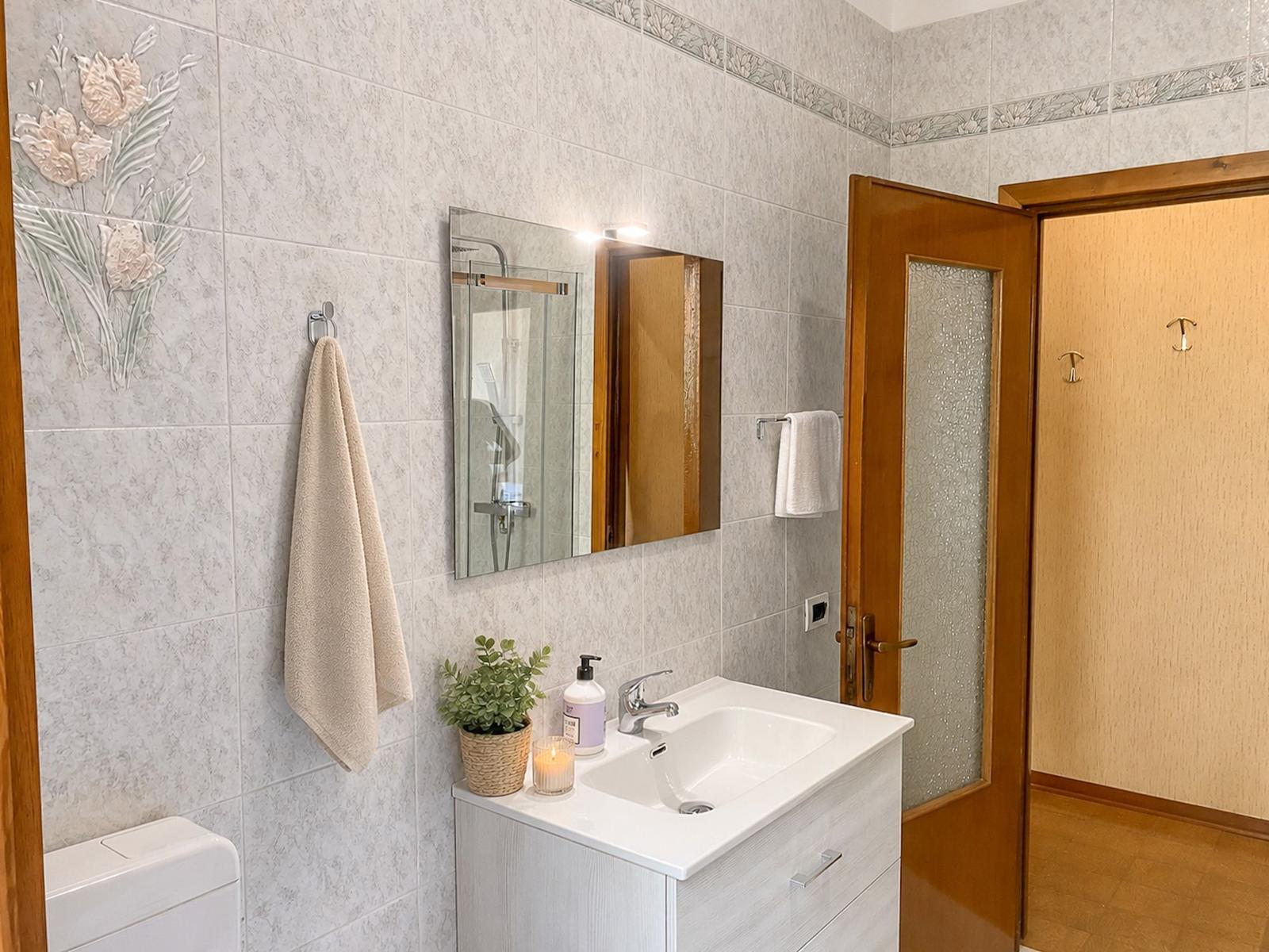 Bathroom with sink, mirror, shower, and toilet. Walls with floral tile pattern.