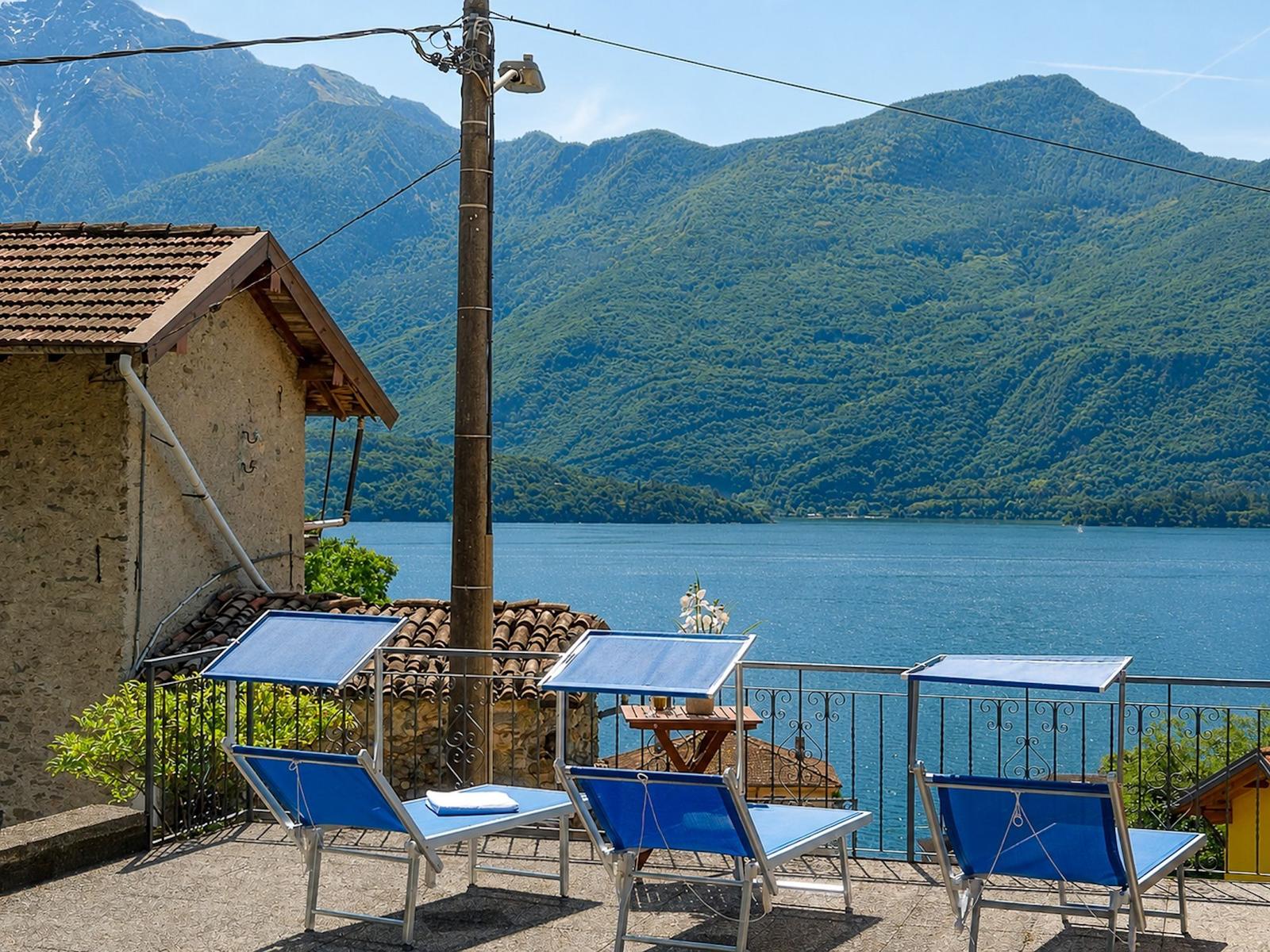 Terrace with three blue lounge chairs and view of lake and mountains.
