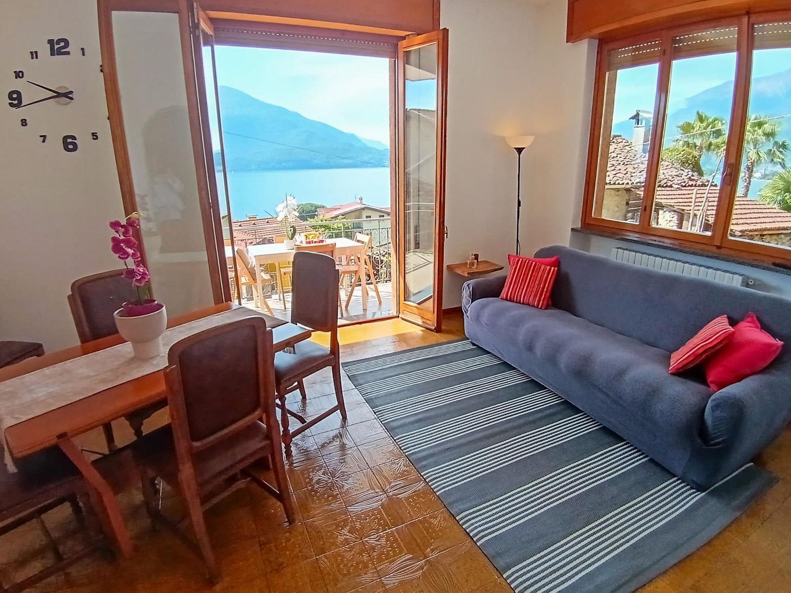 Living and dining area with view of lake and mountains. Sofa, table, and chairs are present.
