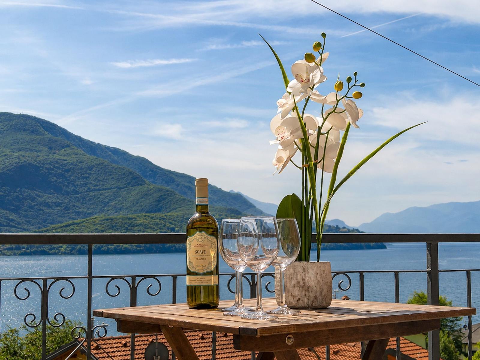 On the terrace, a table with wine, glasses, and an orchid overlooks mountains and lake.