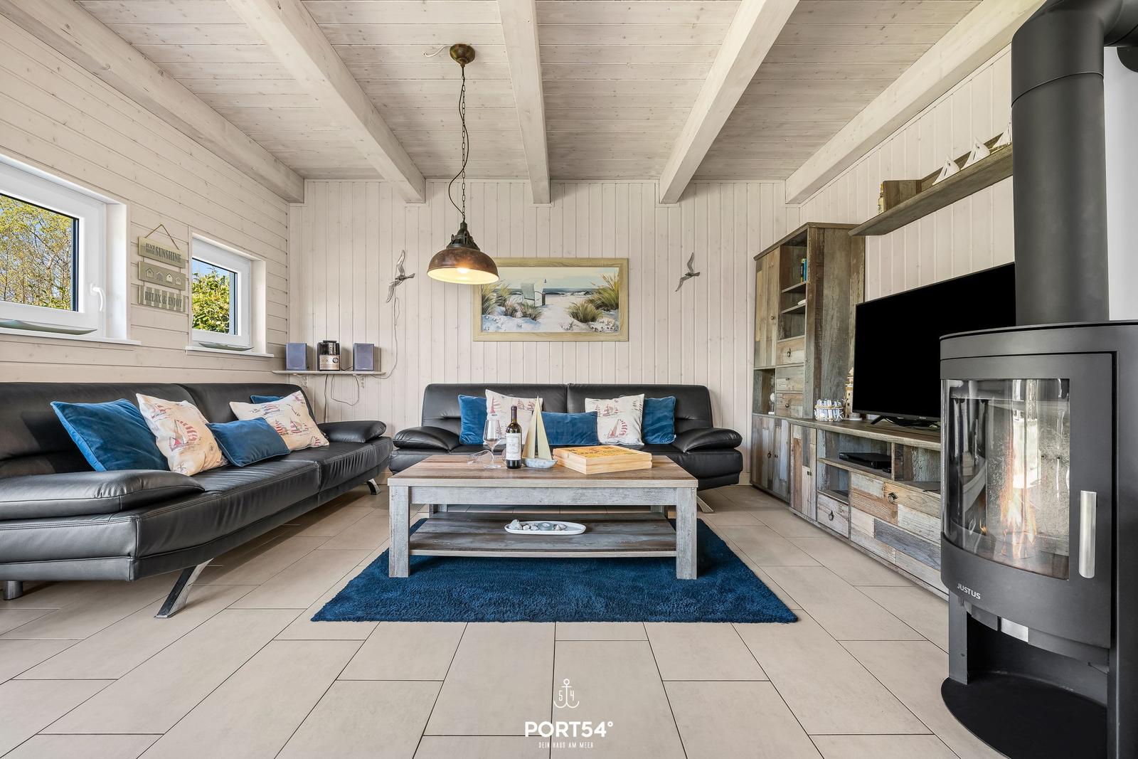 Wohnzimmer mit zwei schwarzen Sofas, Holztisch und Kaminofen. Wandverkleidung und Deckenbalken.
