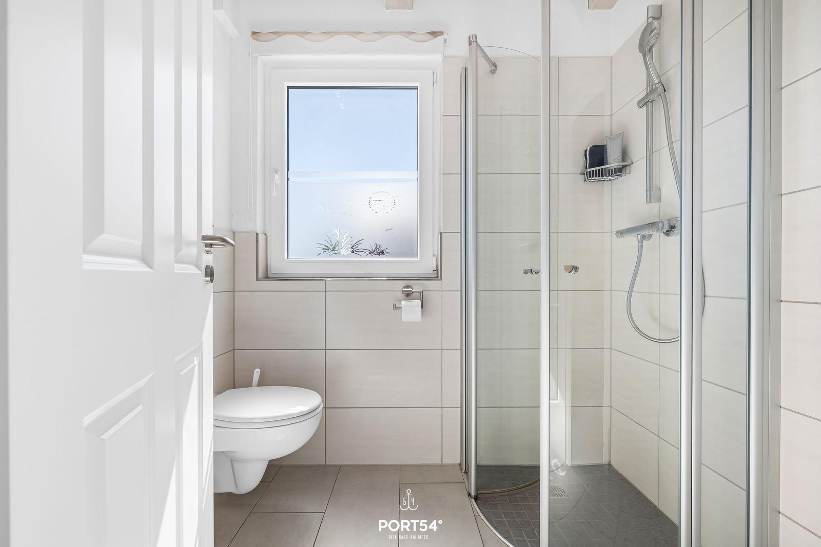 Badezimmer mit Dusche, Toilette und Fenster mit Meerblick.