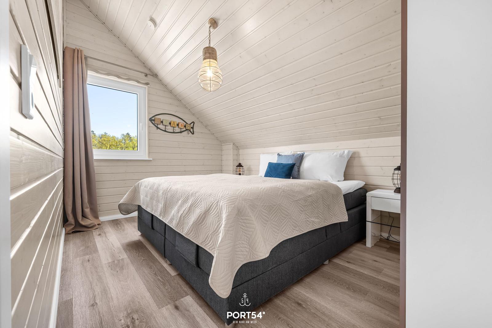 Schlafzimmer mit Dachschräge, Bett, Fenster und Holzboden.